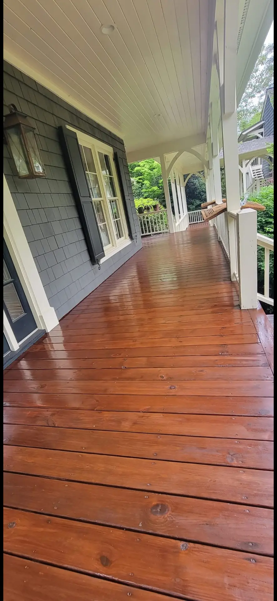 Wraparound porch with freshly stained wood decking and charcoal shake siding